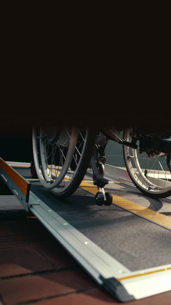 Rollstuhlfahrer steigt über eine seitliche Rampe vom Gehweg in einen Kia WAV ein.